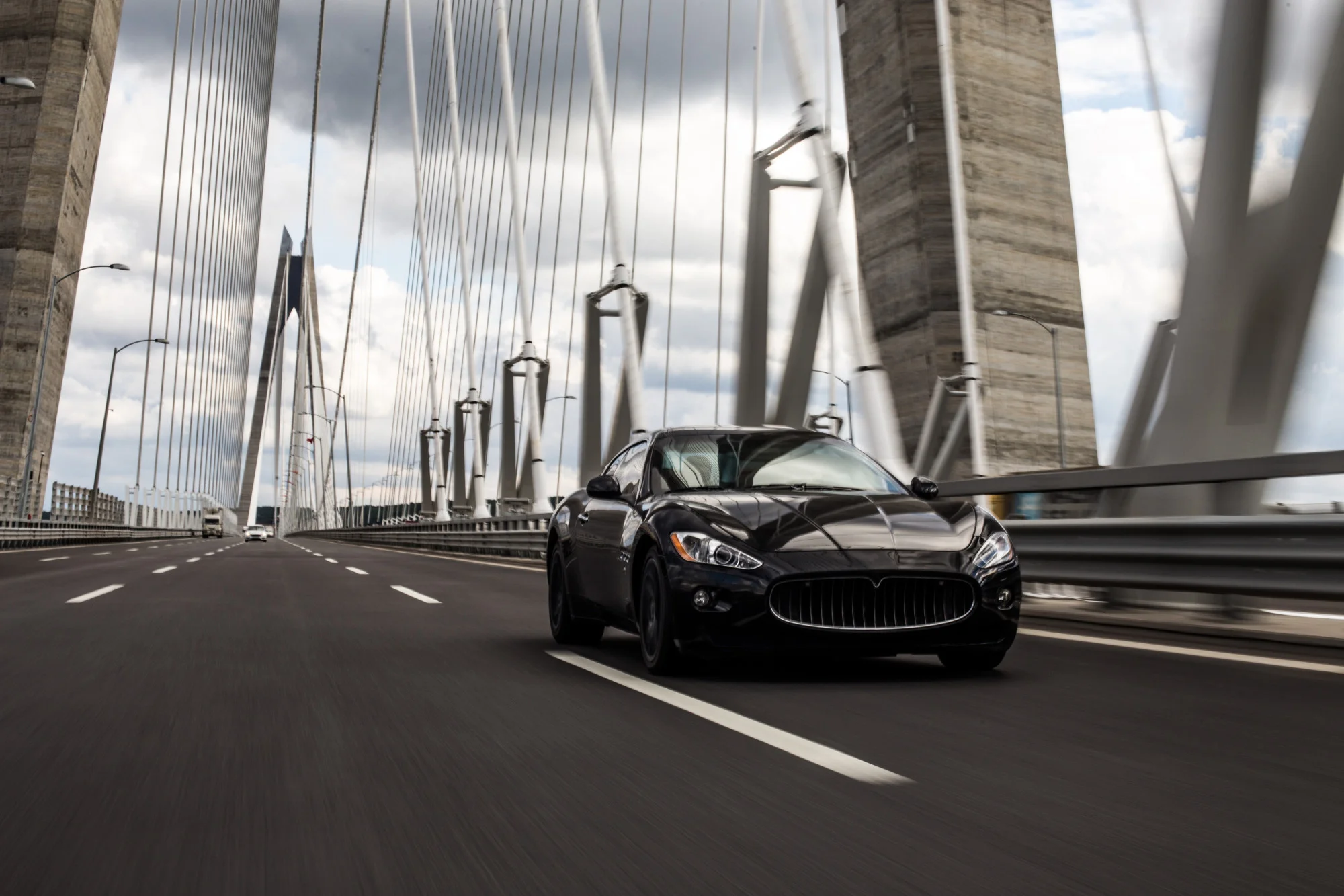 Black sedan travelling across a cable-stayed bridge on an open road